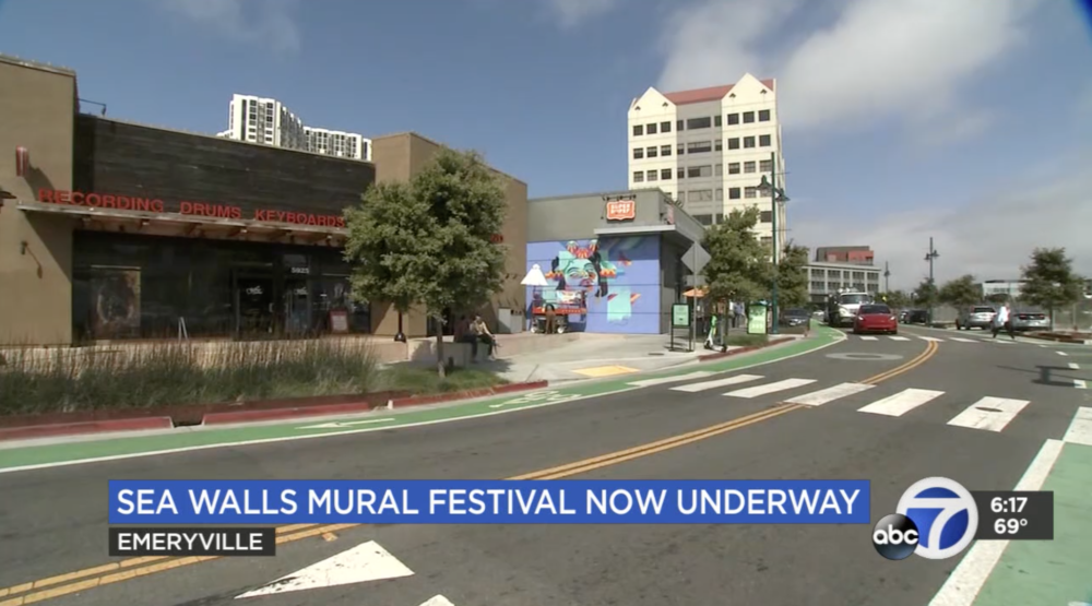 Wide shot of shopping center with artist painting blue mural on exterior wall