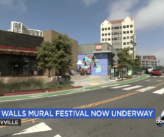 Wide shot of shopping center with artist painting blue mural on exterior wall